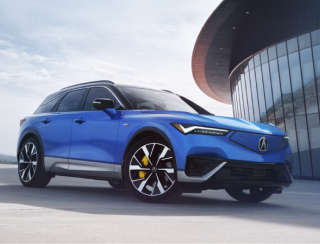 3/4 front view of a blue ZDX parked outside a modern glass-walled building at sunset.