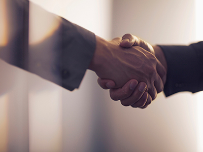 A close-up of two professionally dressed people shaking hands.  / Un gros plan de deux personnes en tenue professionnelle se serrant la main. 