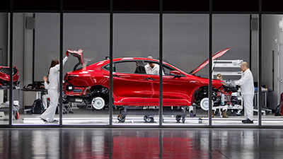 Passenger side view of a red Acura frame on a hoist in a glass-walled room. Acura engineers in white lab uniforms are seen inspecting the vehicle.	Vue du côté passager d’un cadre Acura rouge sur un pont élévateur dans une pièce aux parois en verre. Ingénieurs Acura en sarraus blancs qui inspectent le véhicule.