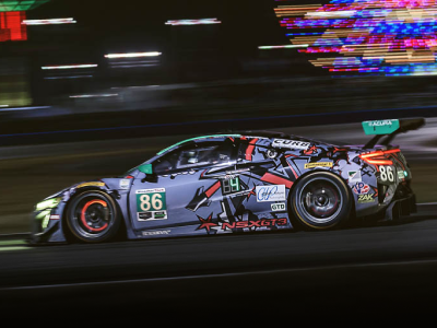 Driver side shot of a purple, sponsorship wrapped Acura NSX GT3 driving at high speed on a racetrack at nighttime.	Vue du côté conducteur d’une Acura NSX GT3 recouverte de logos de commanditaires roulant à haute vitesse sur un circuit de course la nuit.