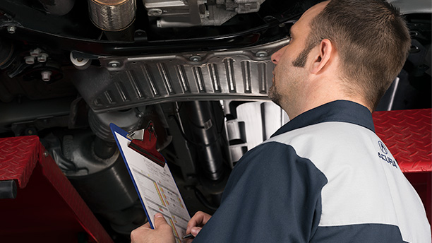 An Acura technician inspects the underside of a vehicle. / Un technicien Acura inspectant le dessous d’un véhicule.
